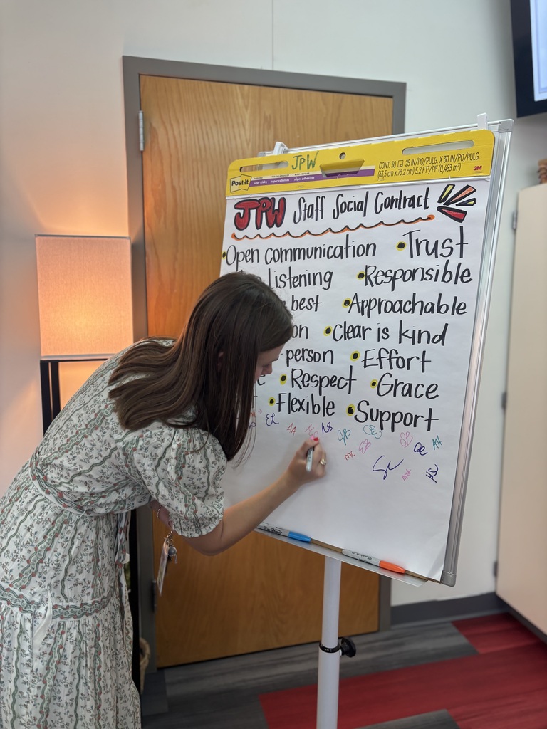 A person writes on a whiteboard titled "Staff Social Contract" with bullet points. The whiteboard stands on a metal stand.