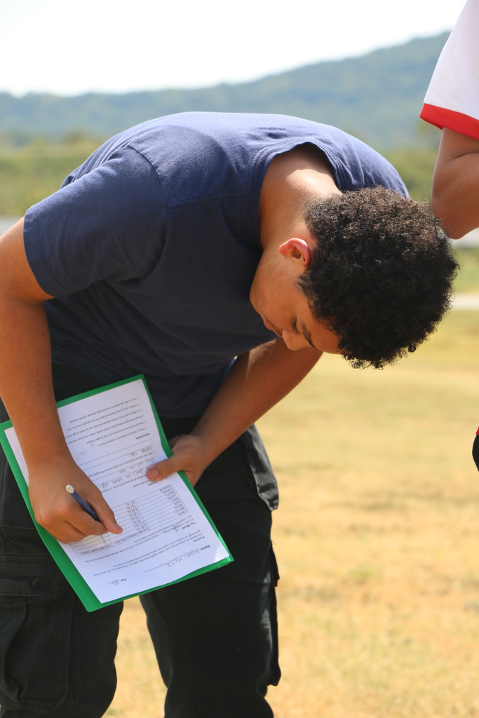 A person wearing a navy shirt and black pants holds a clipboard, writing on a piece of paper.