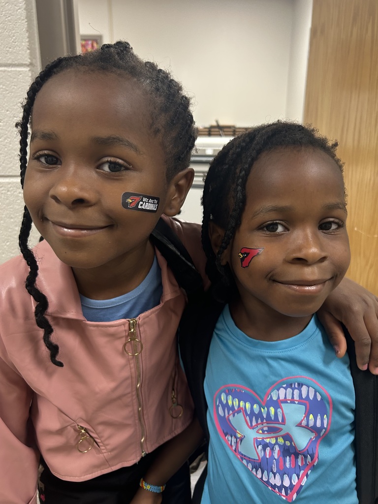 Two girls, one with a face sticker and the other with face paint, smile in a room.