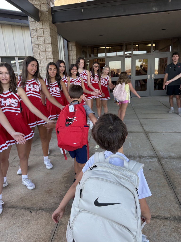 A group of young girls in red uniforms walk in front of a building with a boy in a backpack.