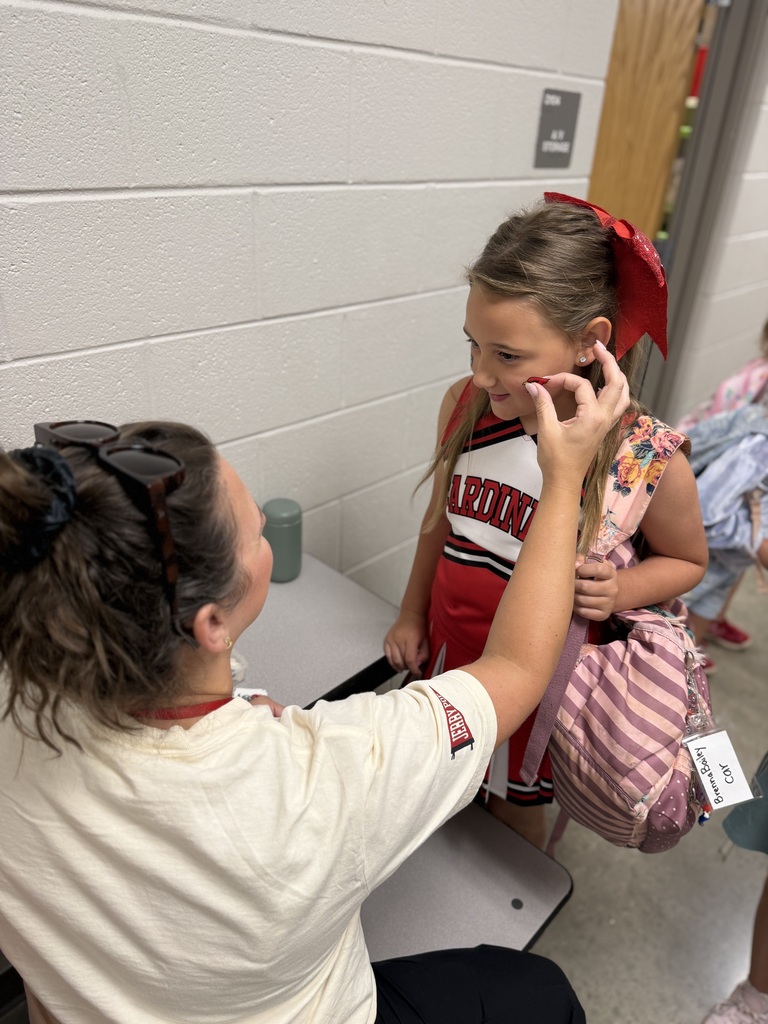 Adult with glasses on head holds young girl's face with hand, girl wears red cheer uniform.