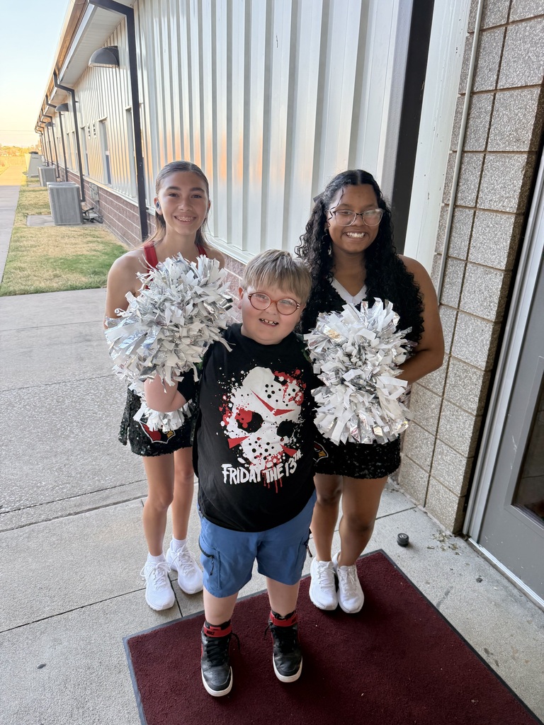 Three individuals pose with pom-poms in front of a building, one holding a small child.