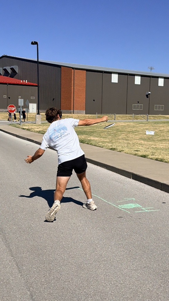 A person stands on a street, reaching for a frisbee, with a building in the background.