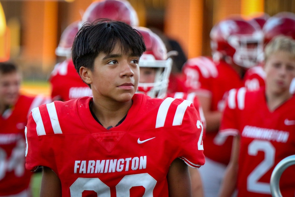 A young football player with the number 00 wears a red Farmington jersey, standing among teammates in red helmets.