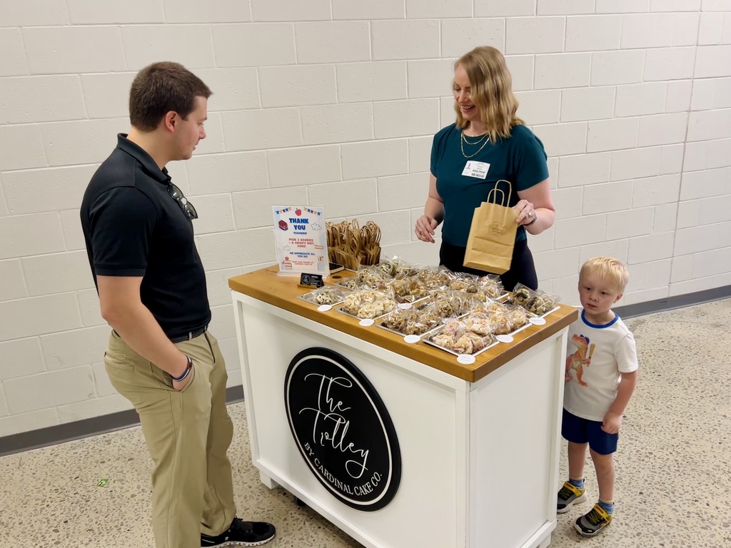 A woman, a man, and a child stand before a table of food with a sign reading "The Jelly."