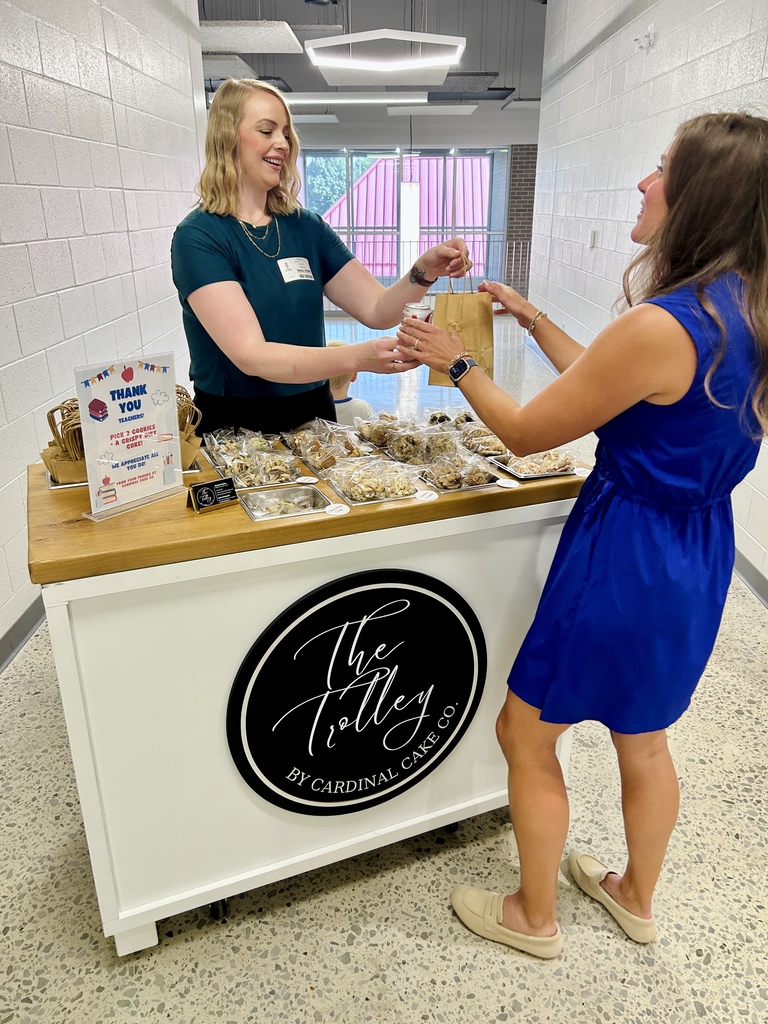Two women, one in green, the other in blue, are standing before a food table.