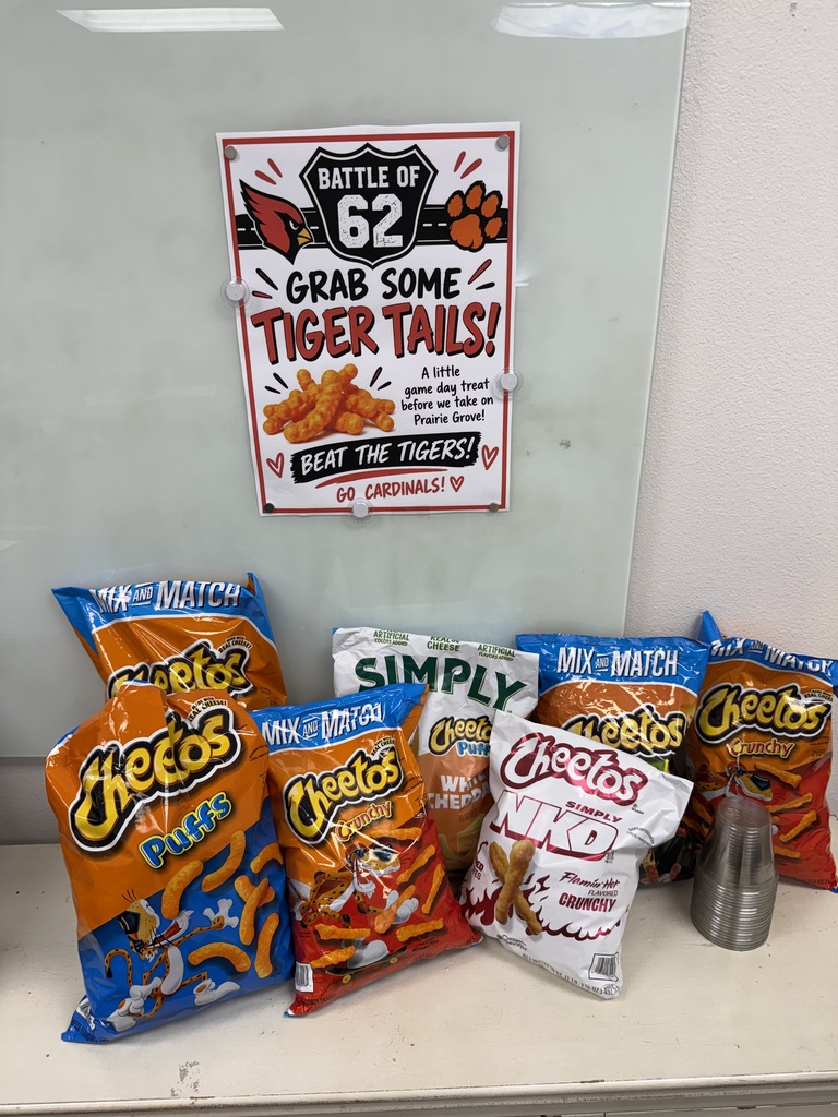 Several bags of snacks including Cheetos, Simply, and Match placed on a shelf. A sign with Battle 62 and Tiger Tails written on it is above the snacks.