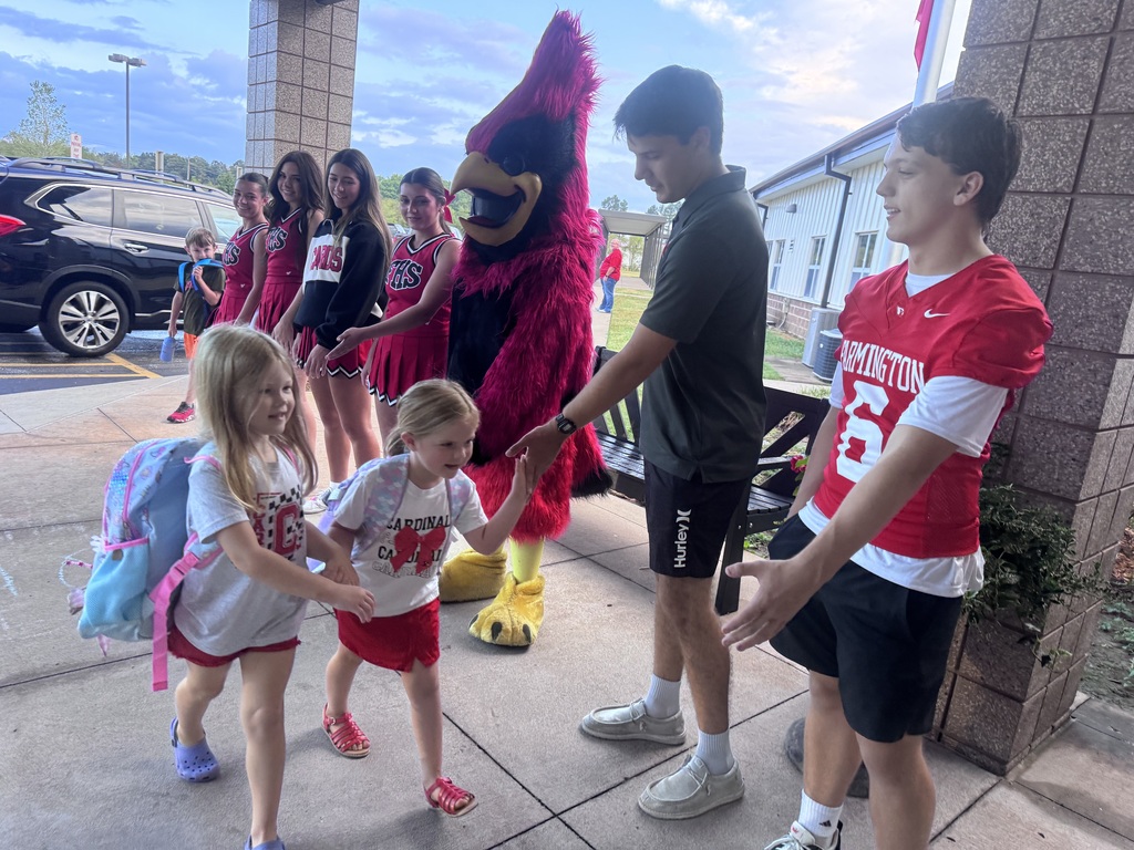 Kids greet a mascot while a man holds hands with two children and another stands nearby.