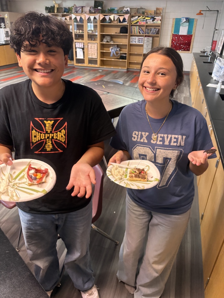 Two children, one wearing a black shirt and the other a blue shirt, hold plates of food.