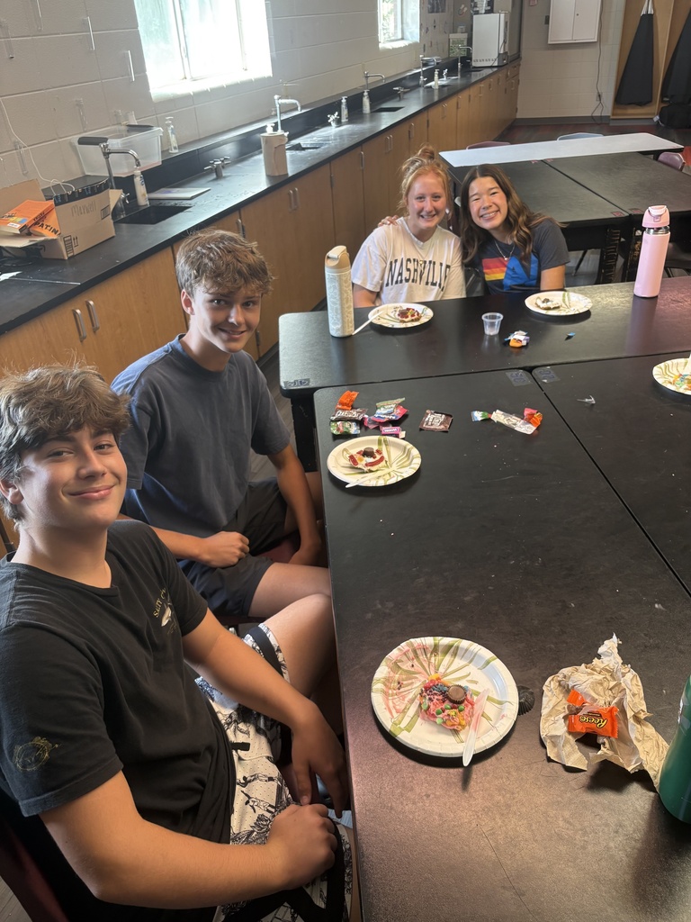 Four students seated at a table in a lab. One student wearing a blue shirt, others in gray.