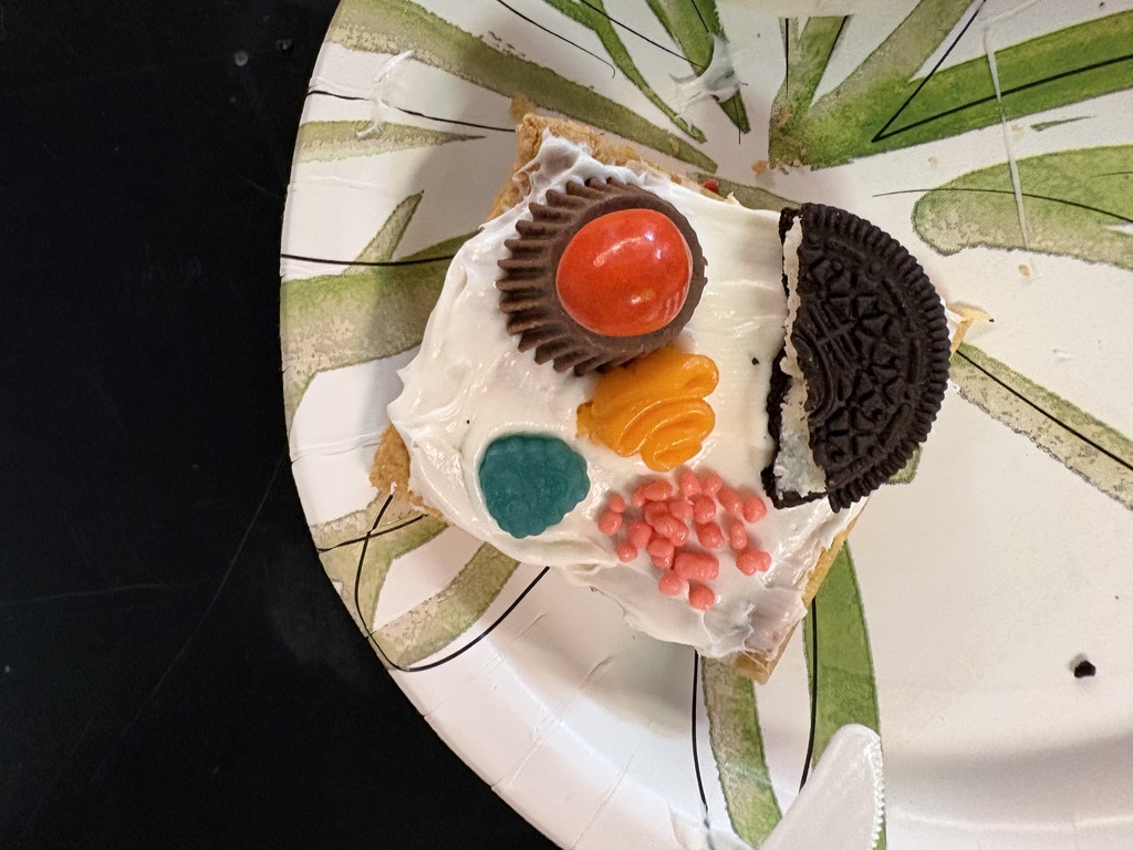 A slice of cake on a plate with a green leaf design, topped with frosting, an Oreo, and colorful candies.
