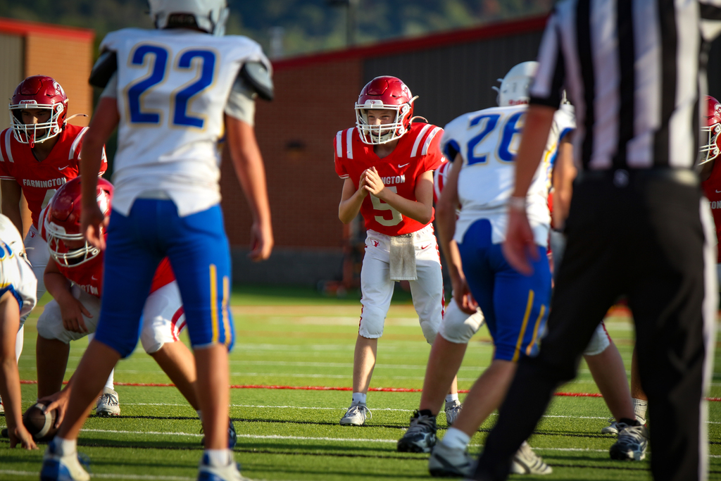 Athletes in football gear on a field. A referee and a player wearing red and white uniforms.