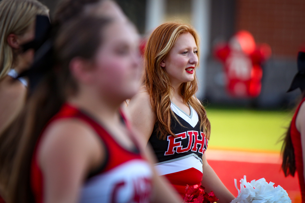 Several cheerleaders in red and white uniforms sit in a row, with one holding pom poms.