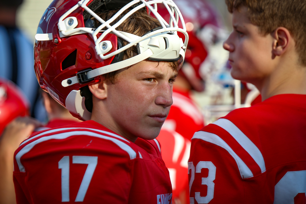 Two football players in red jerseys face each other. Player 17 wears a red helmet with white faceguard. Player 23 wears a red jersey with white stripes.