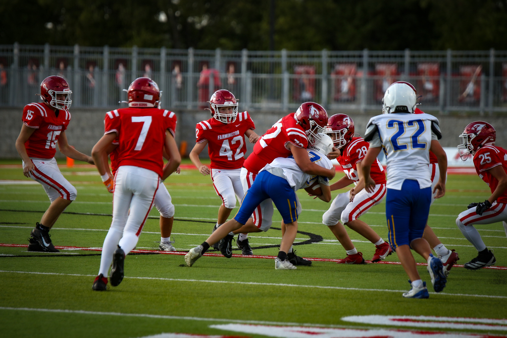 Several football players in red, white, and blue uniforms play on a field with green grass and white markings.