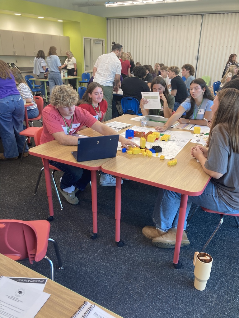 A room with tables and chairs where people are seated and playing with Legos.
