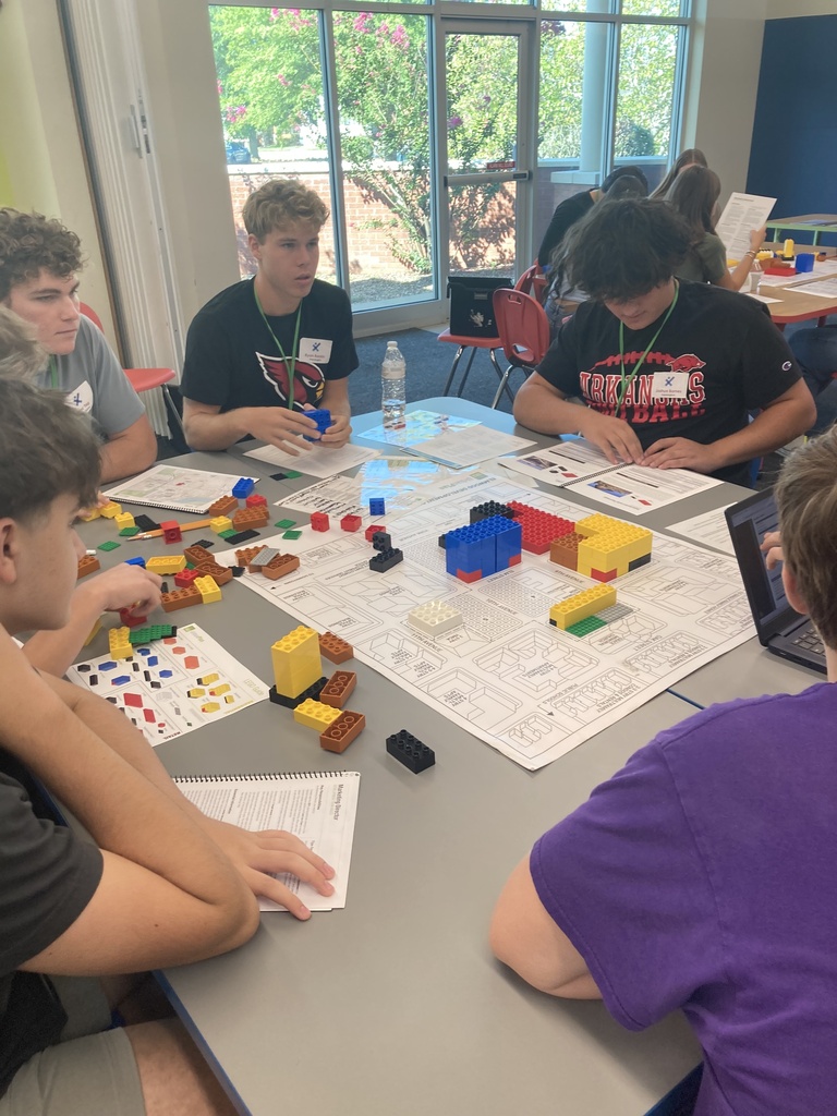 A group of students sits around a table, engaged in an activity with various colored building blocks.