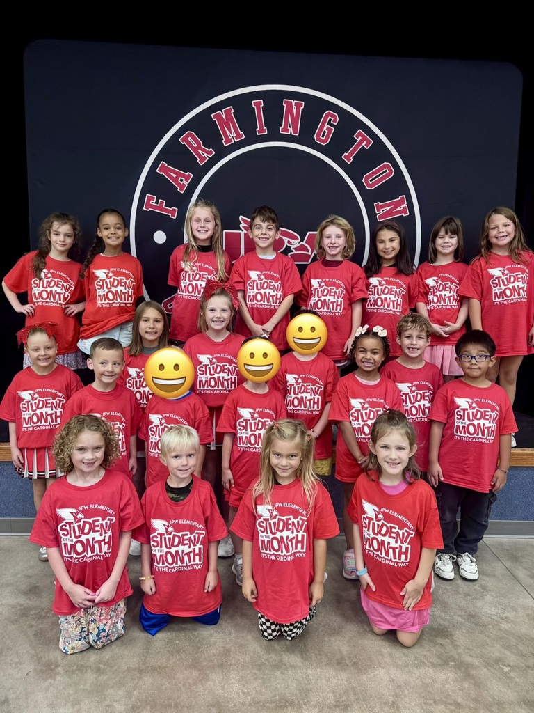 A group of children in red shirts, some with glasses, pose for a photo in front of a blue sign with a logo.