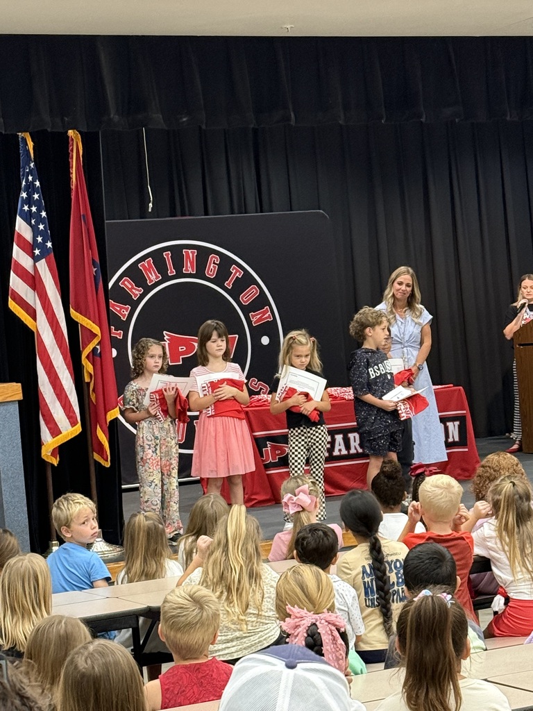 Students on stage holding papers with a flag and podium in the background.