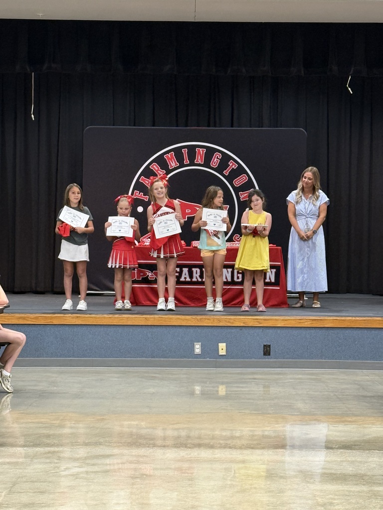 Six children stand on stage holding certificates, a woman stands beside them, and a large black backdrop.