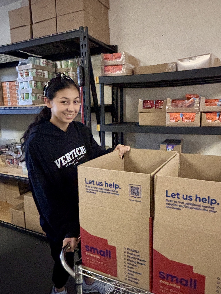 Woman in a black sweatshirt holds two boxes labeled Small, standing next to a shelf filled with boxes.