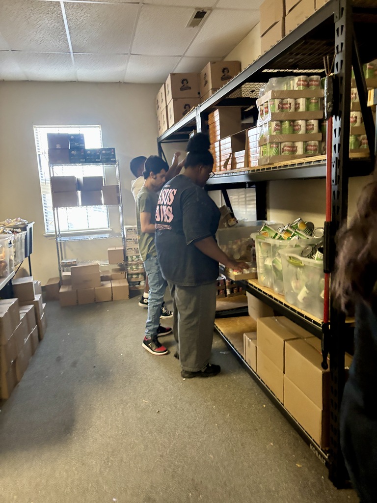 A group of people in a room, examining items on shelves. Boxes are stacked on the floor.