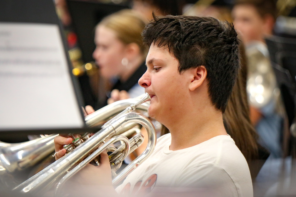 A student plays a trumpet while in a school band, with blurred band members behind him.