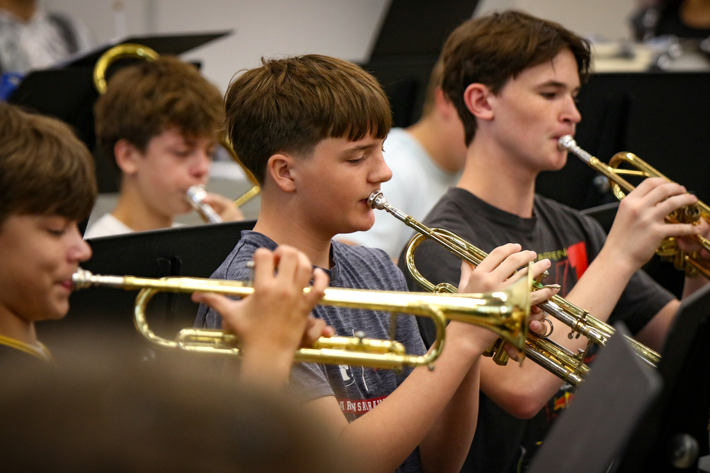 Four boys play trumpets in a band setting; two are in the foreground, and two are in the background.