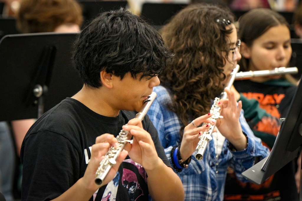Students in a classroom playing flutes with sheet music in front of them.