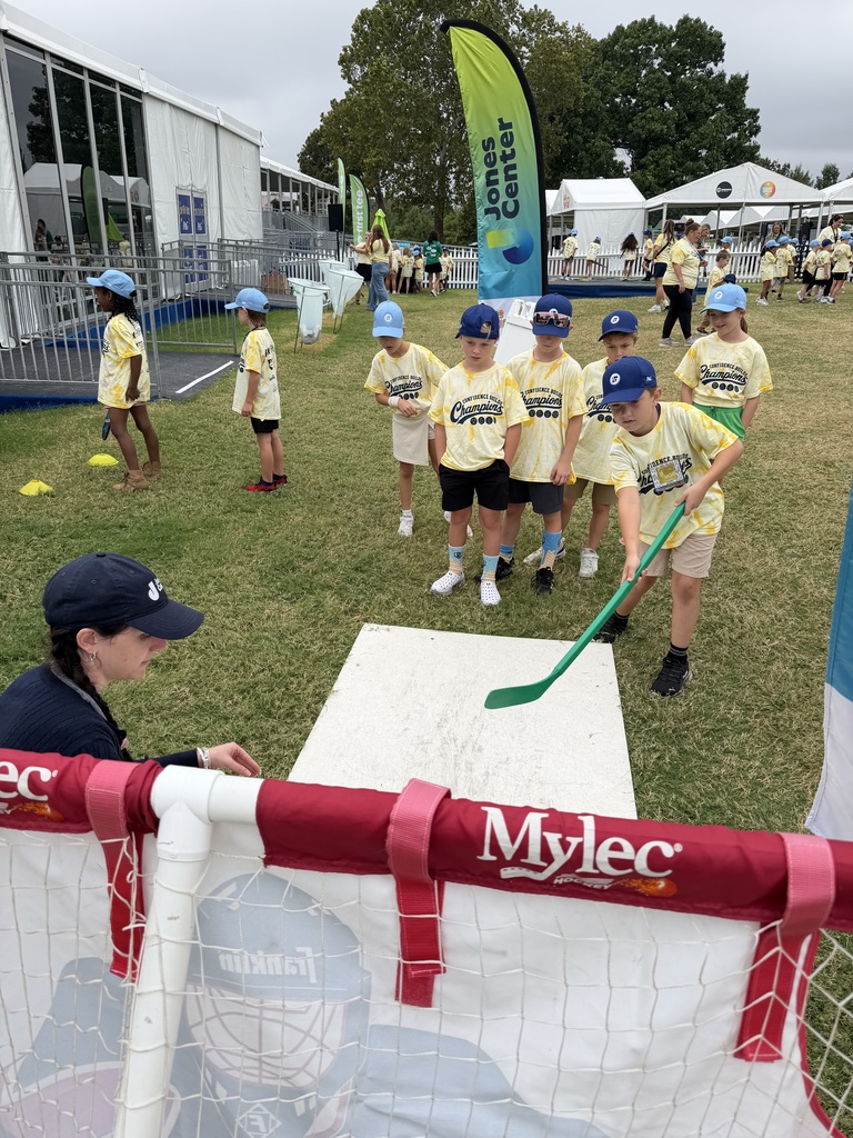 Children in yellow uniforms and caps participate in a hockey activity. A Mylec banner is in the foreground.