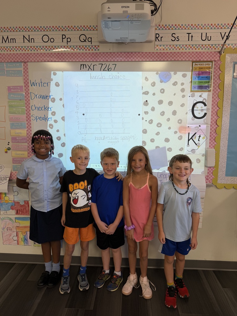 Five children in school uniforms stand together in front of a classroom screen with an educational projector.