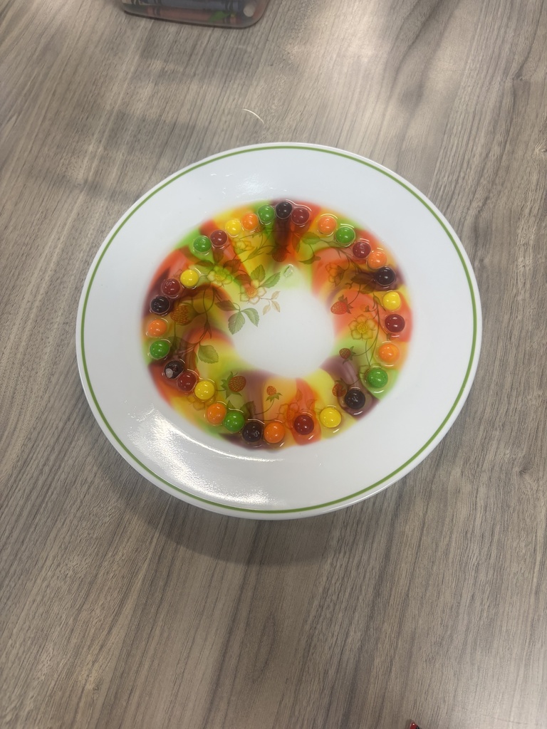 A plate with a colorful ring of candies sits on a wooden table. The plate has a white rim.