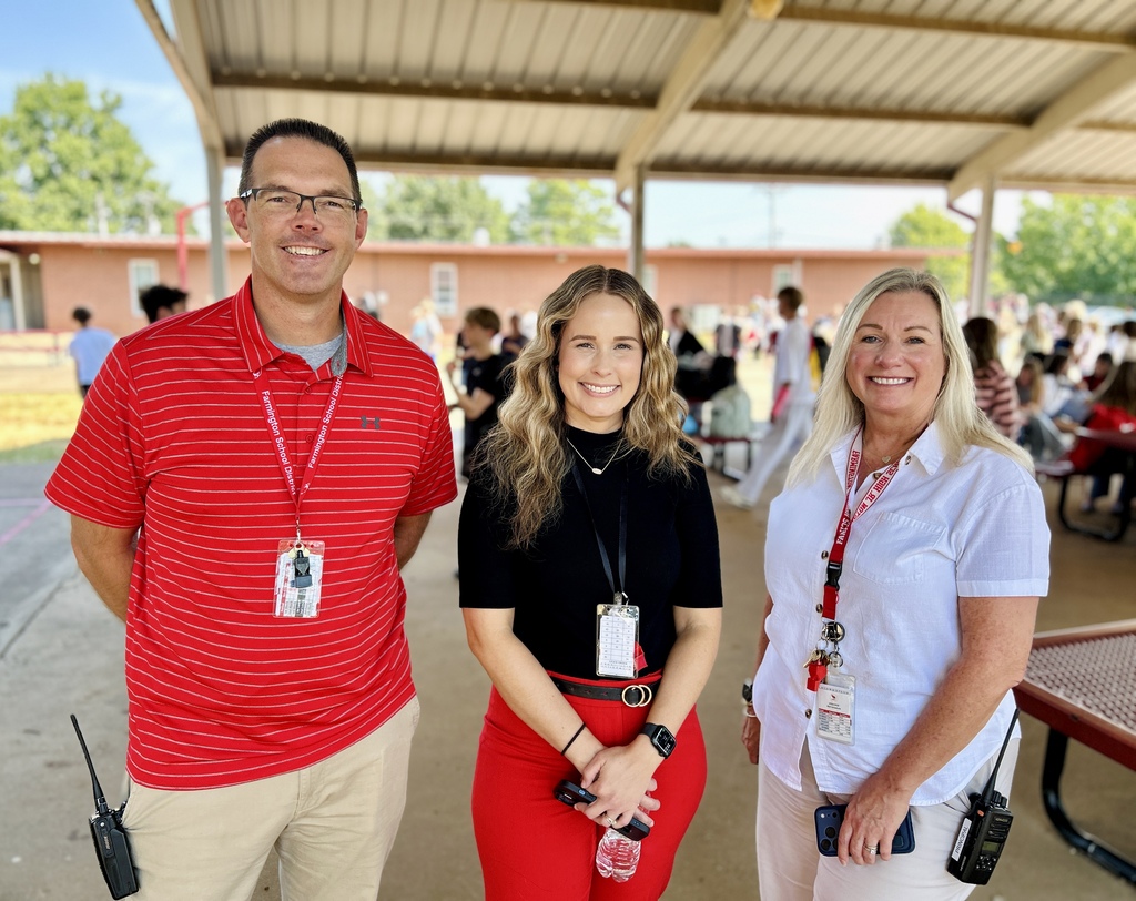 Three people in a covered area, possibly at an outdoor event. A man and two women are standing.