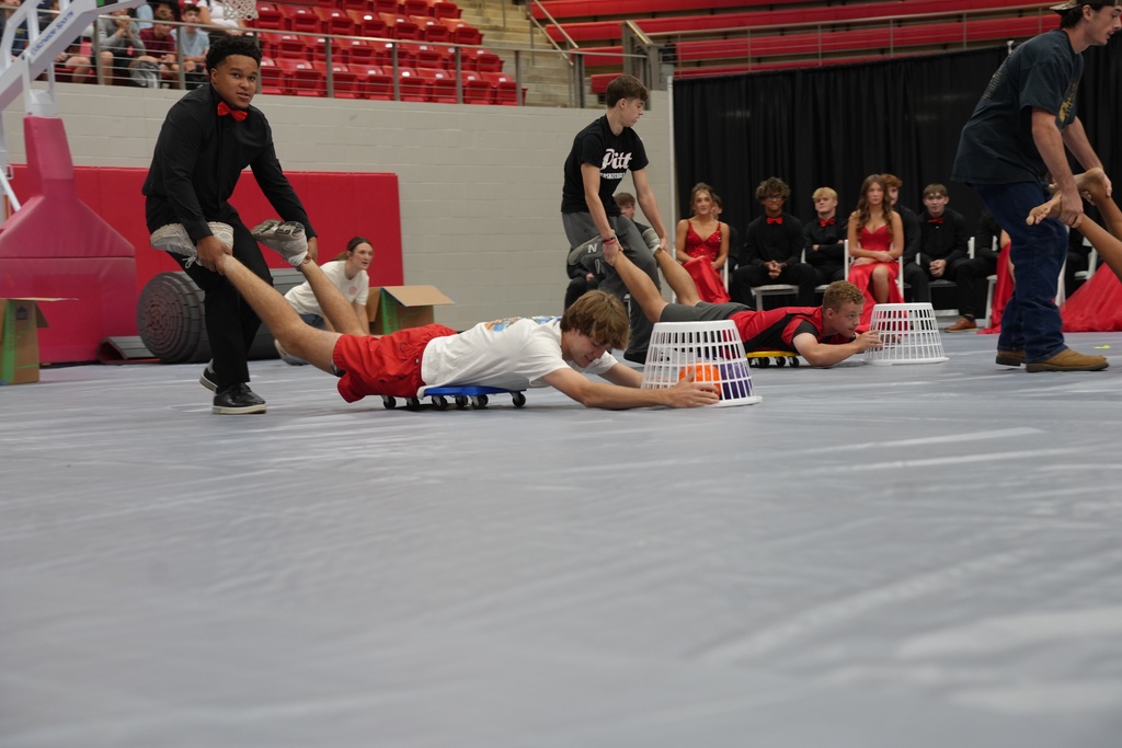 People compete on a mat in a gymnasium. One person slides while others sit or stand nearby.