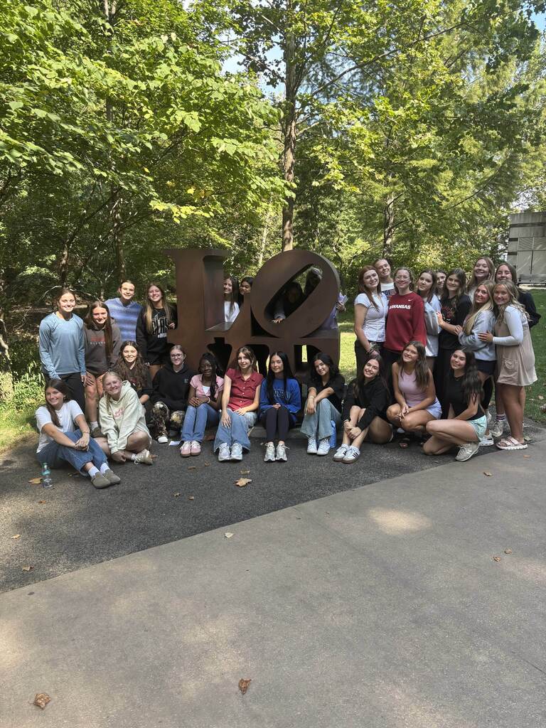 A group of people in casual clothing pose for a picture in front of a large sculpture.
