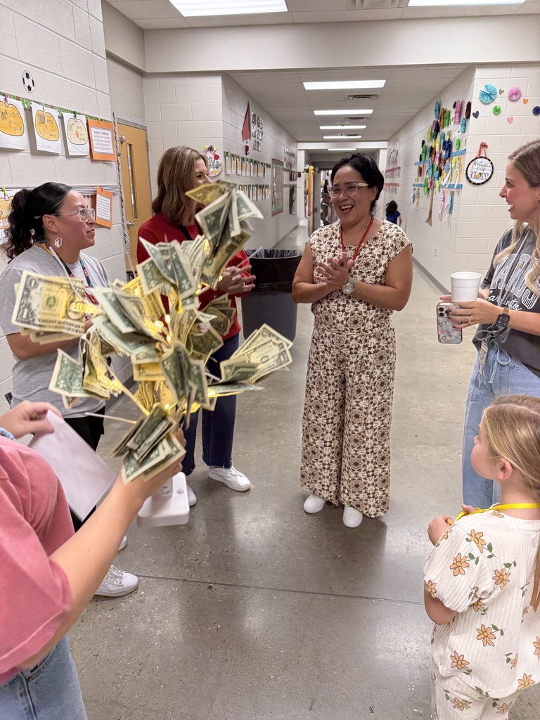 A group of adults and children stand in a hallway, one adult holds a bundle of money.
