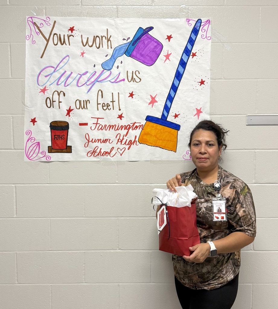 A woman stands in front of a wall with a banner that reads "Your work sweeps us off our feet!"