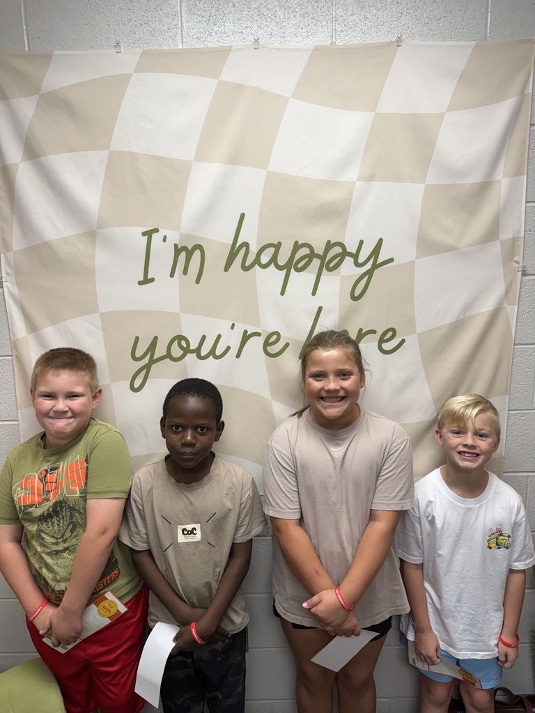 Four children in matching t-shirts stand before a wall with a checkerboard banner that reads "I'm happy you're here."