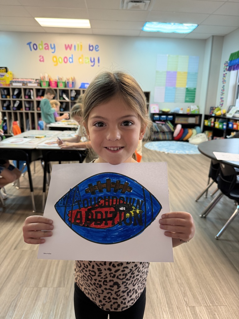 A young girl smiles, holding up a paper with a drawn football and the word "Addie" in blue.