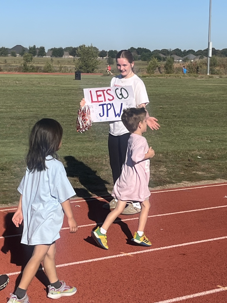 People on a track. A woman holds a sign that says "Let's go JPW." Two children walk next to her.