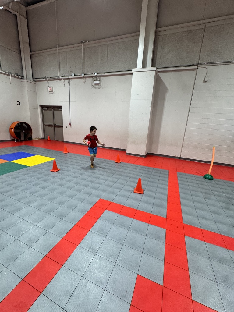 A young child runs on a floor with red, gray, and yellow tiles and orange cones in a large room.