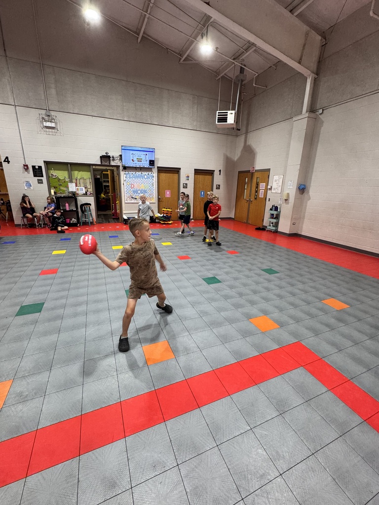 A child throws a red ball in an indoor gym with a tiled floor and a red line.