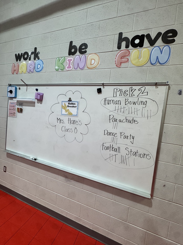 A whiteboard displays colorful text "work hard be kind have fun" against a white brick wall. Below it, there's a list of activities and events.