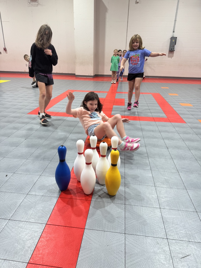 Children playing in an indoor bowling area with bowling pins scattered on a red and gray floor.