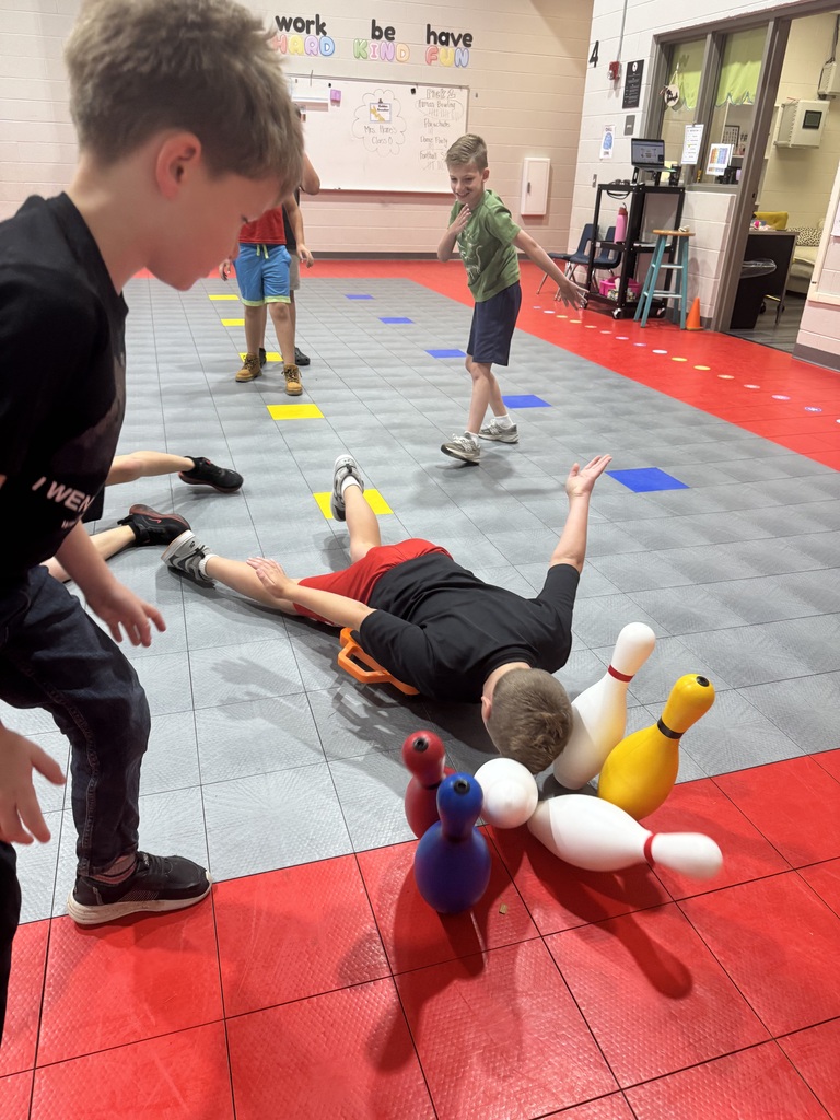 A group of children playing with bowling pins on a colorful floor mat. Some children lie on the floor.