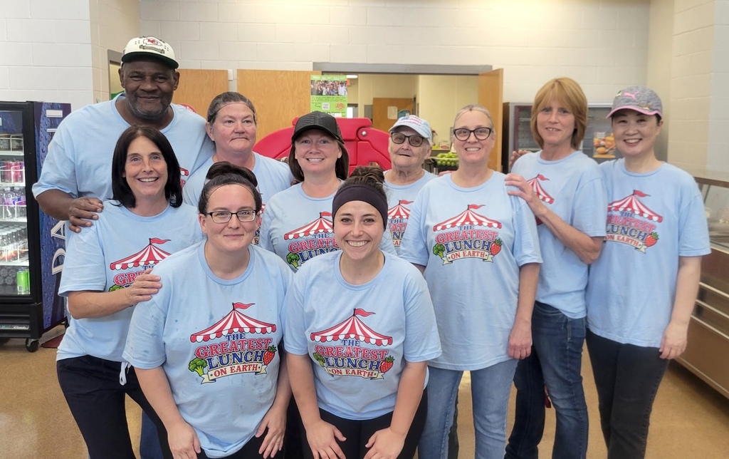 Volunteers in matching blue t-shirts and hats pose for a picture in a room with a refrigerator.
