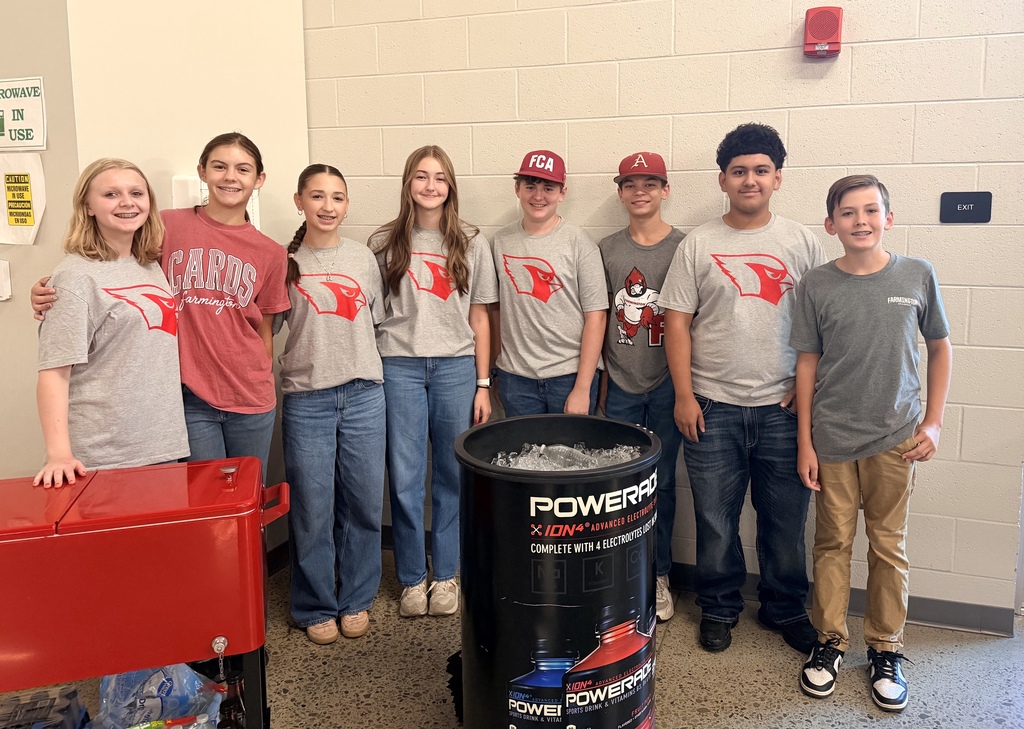A group of people wearing gray t-shirts with red logos pose in a room with a red cooler.