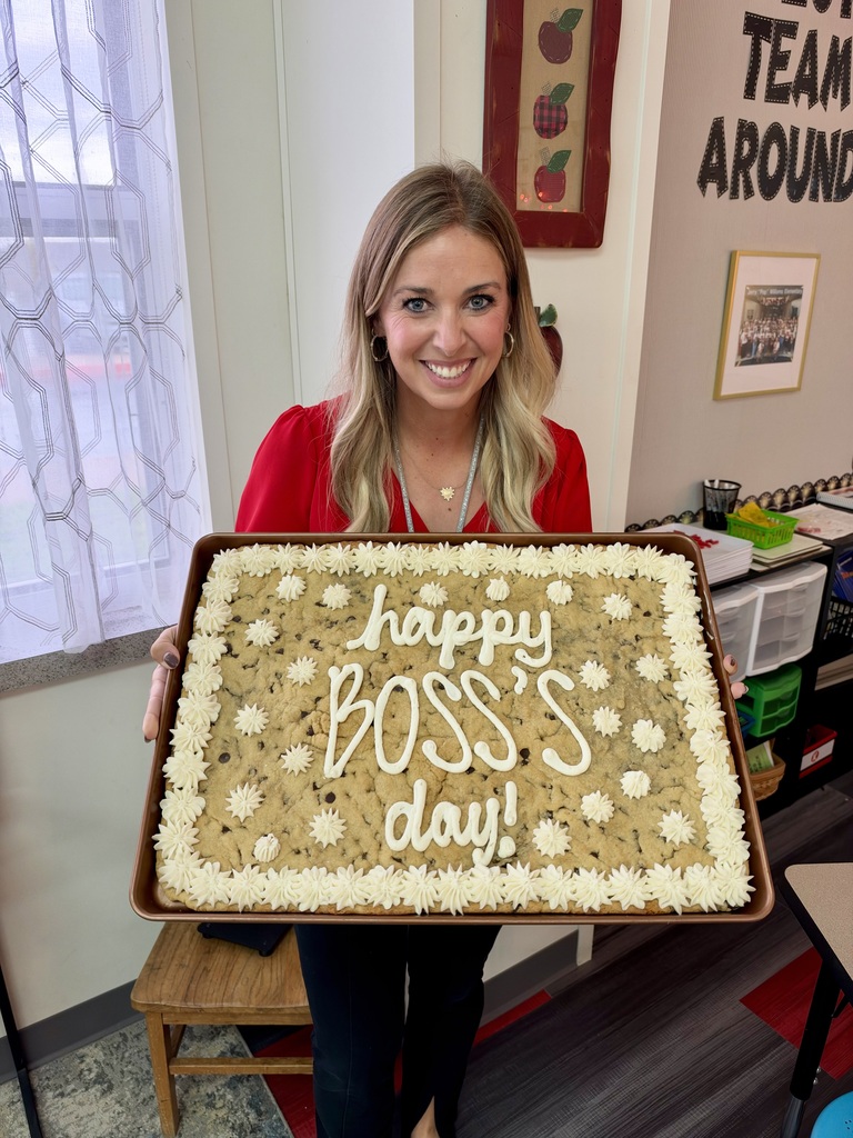 Woman holds a large cookie cake with white icing saying "happy boss's day!" in an office.