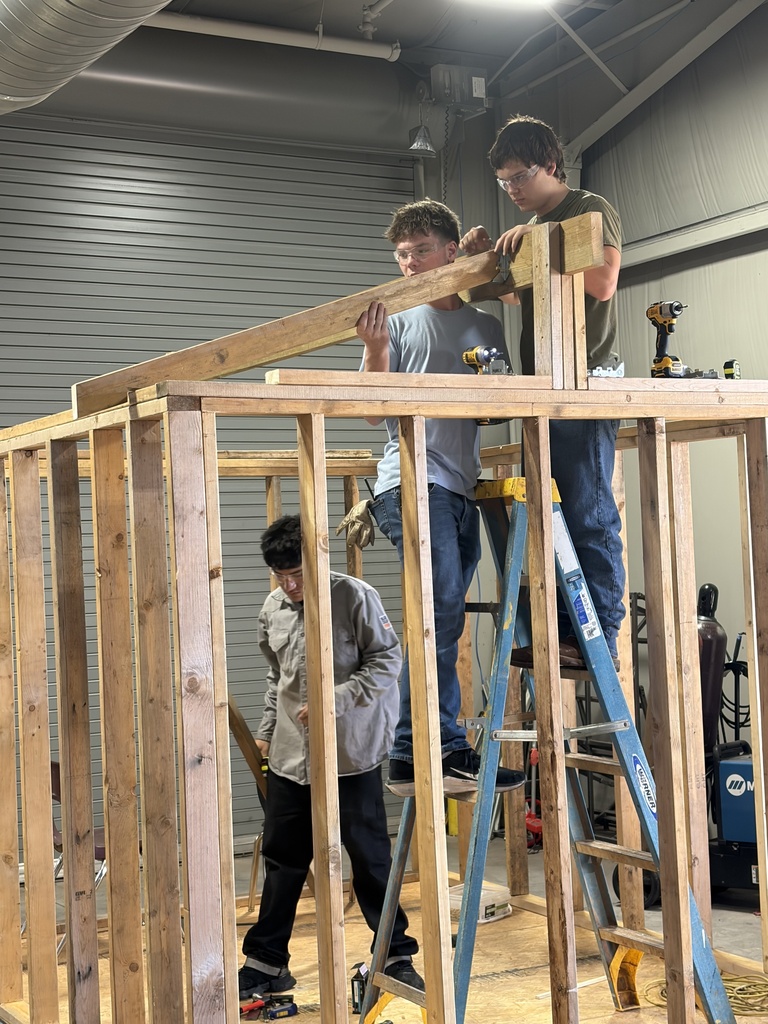 Three men are constructing a wooden structure in a garage. One man is standing on a ladder.