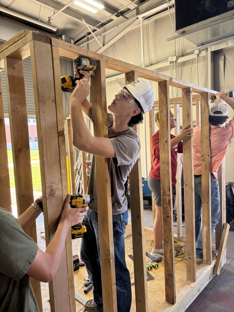 A group of people wearing helmets and holding tools. One is drilling while another is standing nearby.